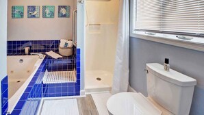 Et badeværelse med badekar, toilet og bruser. Fire billeder hænger på væggene, og et vindue har foldegardiner.
