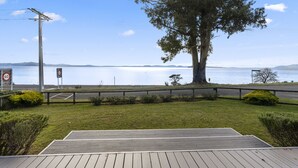 A wooden deck overlooking a calm lake with a large tree in the foreground and a speed limit sign in the background. - Waitetoko Waterfront - Waitetoko Holiday Home (Waitetoko)