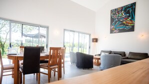 A modern living room with a dining area, large windows, and a colorful abstract painting.