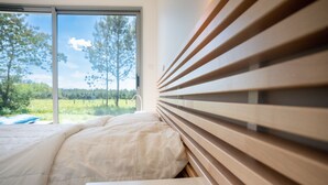 A bedroom with a large window, a bed with white bedding, and wooden slats on the headboard.