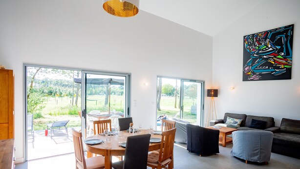 A modern living room with a dining area, large windows, and a colorful abstract painting.