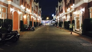 A row of brick buildings with balconies, a paved street, and a few parked motorcycles. - Phuket Racha Guesthouse (Karon)