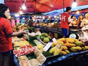 Un puesto de mercado con diversas frutas y verduras, incluyendo mangos, piñas y bananas.