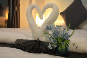 Una cama con una toalla dispuesta en forma de corazón y un jarrón con flores.