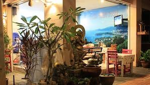 A restaurant with outdoor seating, potted plants, and a view of the sea. - Phuket Racha Guesthouse (Karon)