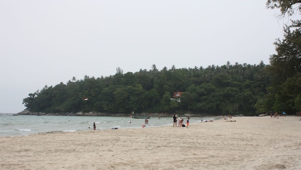 A beach with people, a boat, and a forested hill in the background. - Phuket Racha Guesthouse (Karon)