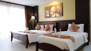 A hotel room with two beds, each with a brown pillow and a white towel. There is a painting on the wall above the beds and a lamp on the nightstand. - Phuket Racha Guesthouse (Karon)
