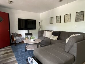 A living room with a grey sofa, a coffee table, a TV, and framed artwork on the wall. - Quaint East Lake House (Spirit Lake)