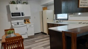 Kompakti keittiö, jossa on valkoiset kaapit, mikroaaltouuni, liesi ja jääkaappi. Keittiössä on puinen ruokapöytä tuoleineen sekä pieni keittiösaareke jakkaroineen.