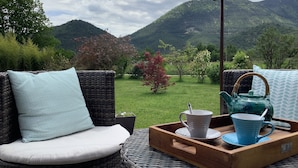 A wicker sofa with a cushion and a tray with a teapot and cups.