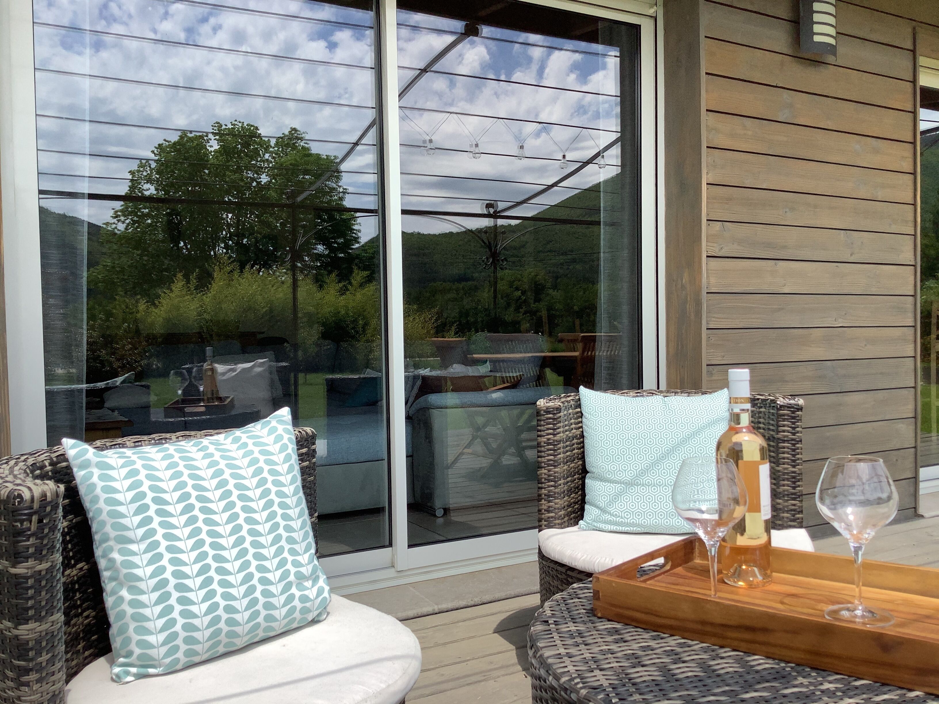 Een terras met rieten meubels, kussens en een dienblad met een fles en wijnglas.