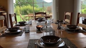 A dining table set for six with a view of a lush garden and mountains in the background.