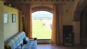 A room with a sofa, a fireplace, and a view of a green field through an arched doorway. - Casa delle Mammole B: A characteristic and welcoming apartment that is part of an ancient country house surrounded by the greenery, with Free WI-FI. (Citerna)