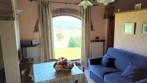 Um quarto aconchegante com uma mesa de jantar, um sofá azul e vista para o exterior através de uma janela com cortinas.