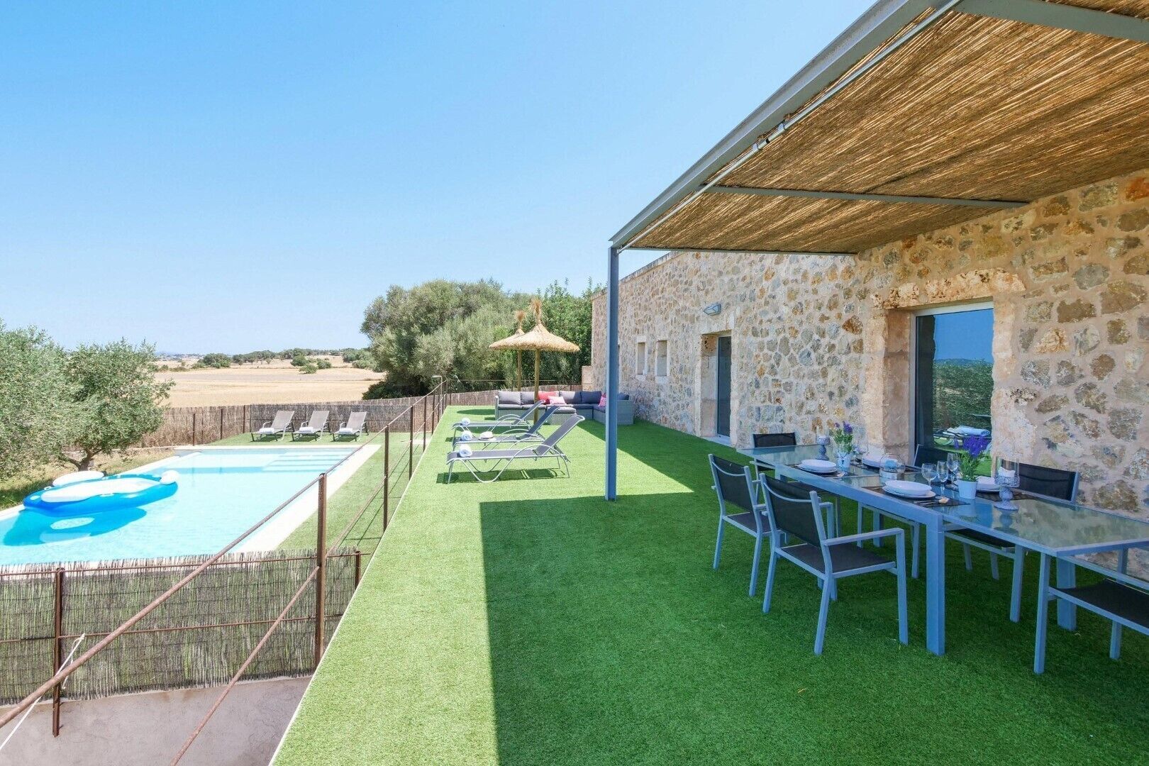 A pool with lounge chairs, a dining table set for two, and a stone building with a view.