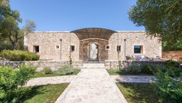 A stone building with a central archway, a paved pathway leading to the entrance, and a garden with shrubs and a small tree. - Holiday Home "Es Gassons" with Pool, Wi-Fi, AC, Terrace & Garden (María de la Salut)