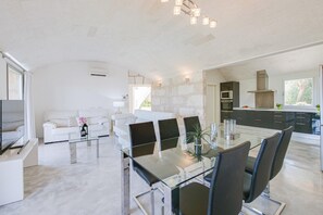 Une cuisine moderne avec des meubles de couleur sombre, un îlot central et un coin repas comprenant une table et des chaises en verre.