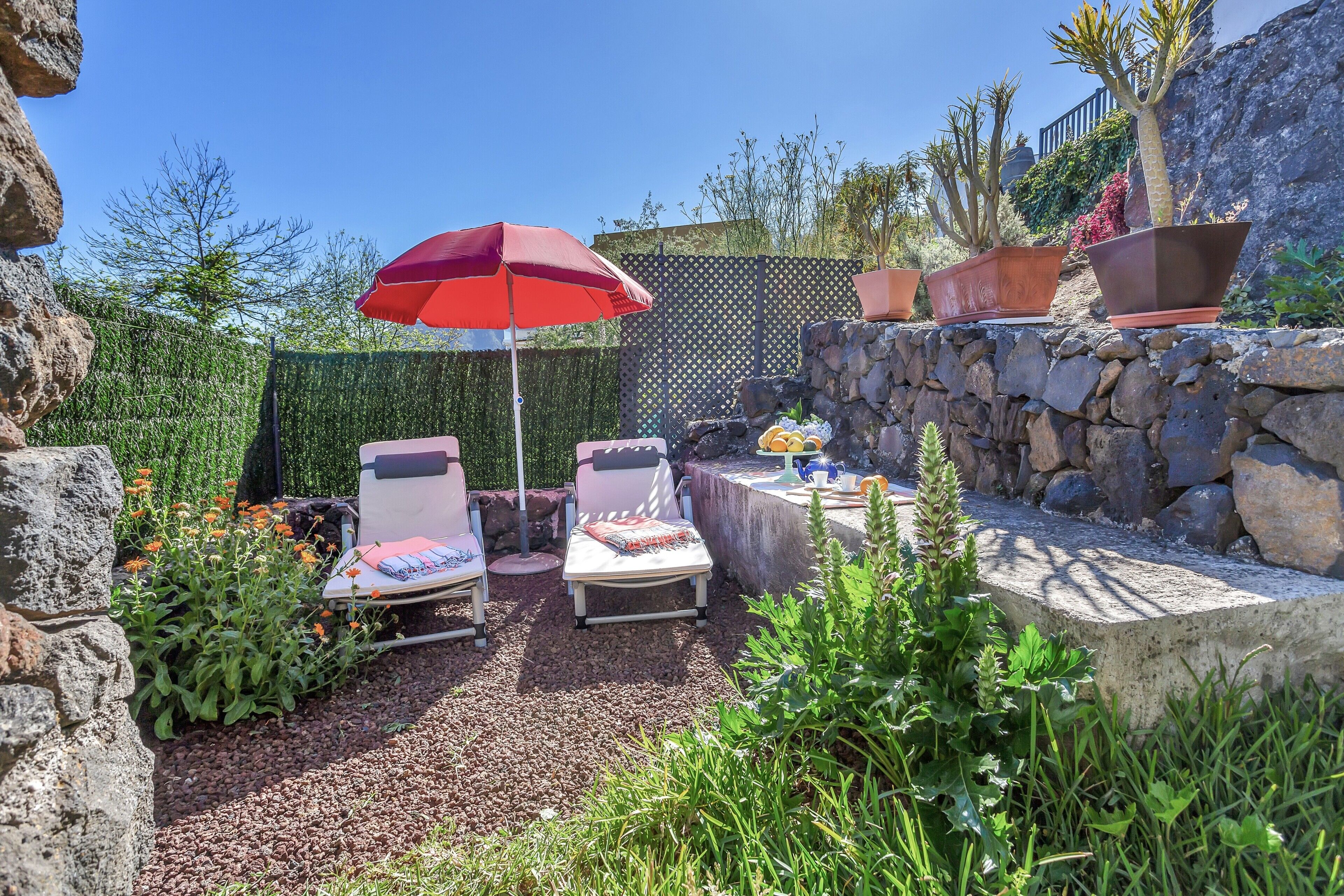 A patio with two lounge chairs, a red umbrella, and a small table with a drink.