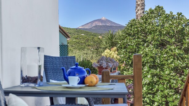 A table with a teapot, cup, and orange, a chair, and a view of a mountain. - Tiled House with Sea & Mountain Views, Wi-Fi, Terrace, Garden, Pet-Friendly (La Orotava)