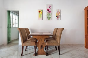 Un coin repas avec une table en bois et quatre chaises, une porte verte et trois tableaux accrochés au mur.