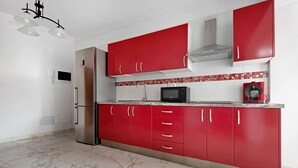 Une cuisine avec des meubles de rangement rouges, un réfrigérateur en acier inoxydable, un four à micro-ondes et une machine à café.