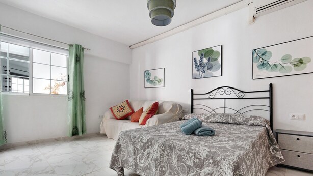 Une chambre à coucher comprenant un lit, une table de chevet, une fenêtre avec des rideaux et des œuvres d’art murales.