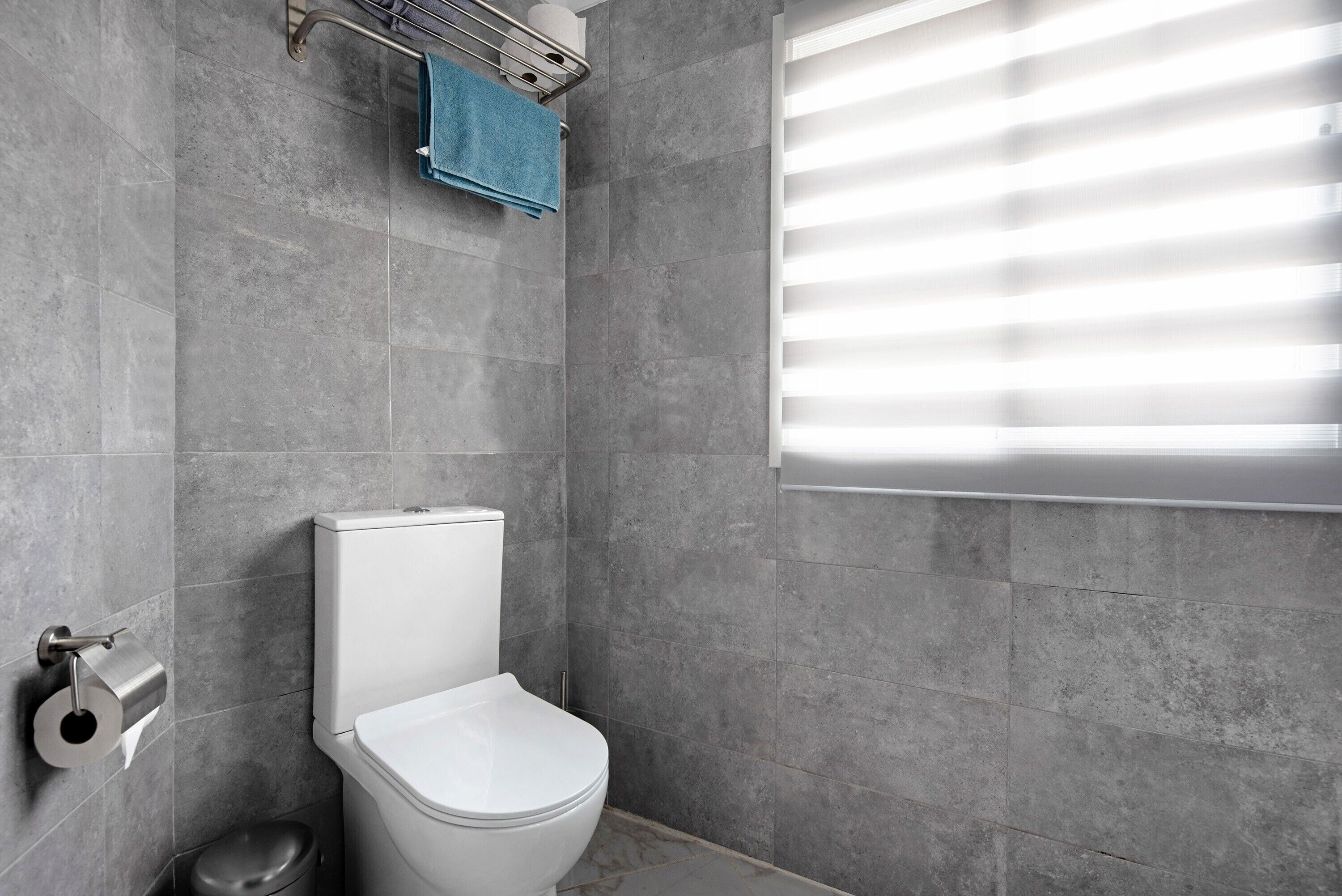Un baño moderno con inodoro, toallero y ventana con persianas.