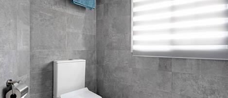 Un baño moderno con inodoro, toallero y ventana con persianas.
