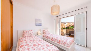 A bedroom with two beds, a nightstand, a lamp, and a view of the outside. - Holiday Home "Villa Sion" with Mountain Views, Pool, Wi-Fi & Terrace, Near Beaches (Cala Mendia)