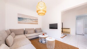 A modern living room with a sectional sofa, two side tables, a hanging light fixture, a flat-screen TV, and a painting on the wall. - Holiday Home "Villa Sion" with Mountain Views, Pool, Wi-Fi & Terrace, Near Beaches (Cala Mendia)