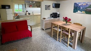 Un espace de vie compact comprenant un coin cuisine, un espace repas avec une table et des chaises, un canapé rouge, un téléviseur et un tableau accroché au mur.