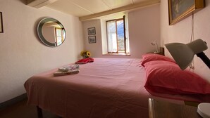 Une chambre à coucher avec un lit, un miroir rond, une fenêtre et un tableau au mur.