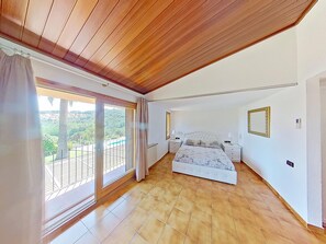 Quarto com cama grande, varanda e vista, e teto de madeira.