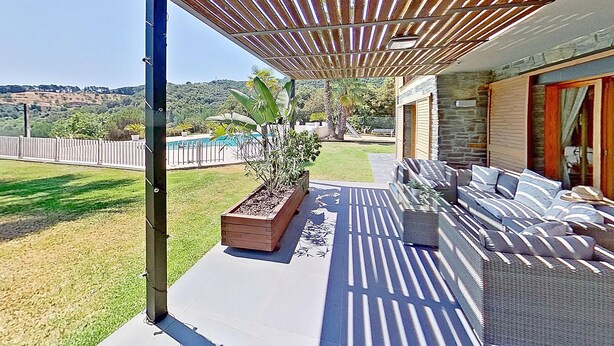 An outdoor patio with a wooden pergola, a seating area with cushions, a planter box, and a view of a swimming pool and hills in the background. - PREMIUM HABITAT CAN FERRER (Arenys de Munt)