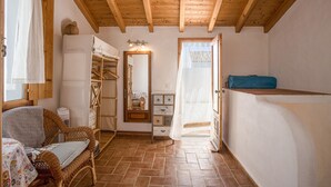 Une pièce avec un plafond en bois, une chaise en osier, un miroir, une armoire et un lit.