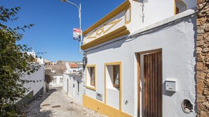 Une ruelle étroite pavée, bordée d’un immeuble blanc avec une porte en bois et une boîte aux lettres.