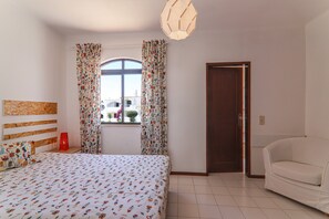 A bedroom with a bed, a window with curtains, a door, and a white sofa. - Villa 'Mourisca' with Shared Pool, Private Garden and Wi-Fi (Alporchinhos)