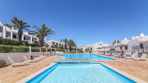 A swimming pool with lounge chairs, palm trees, and white buildings. - Villa 'Mourisca' with Shared Pool, Private Garden and Wi-Fi (Alporchinhos)