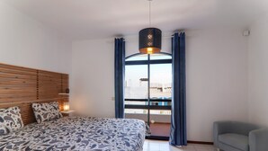 A bedroom with a bed, a sofa, a window with curtains, and a hanging light fixture. - Villa 'Mourisca' with Shared Pool, Private Garden and Wi-Fi (Alporchinhos)