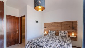 A bedroom with a wooden headboard, a patterned bedspread, a bedside lamp, and a door. - Villa 'Mourisca' with Shared Pool, Private Garden and Wi-Fi (Alporchinhos)