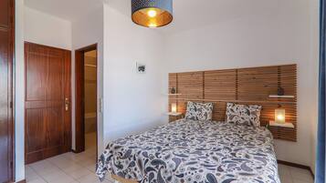 Een slaapkamer met een houten hoofdbord, een bed met een decoratieve spreidekker, een bedlampje en een deur.