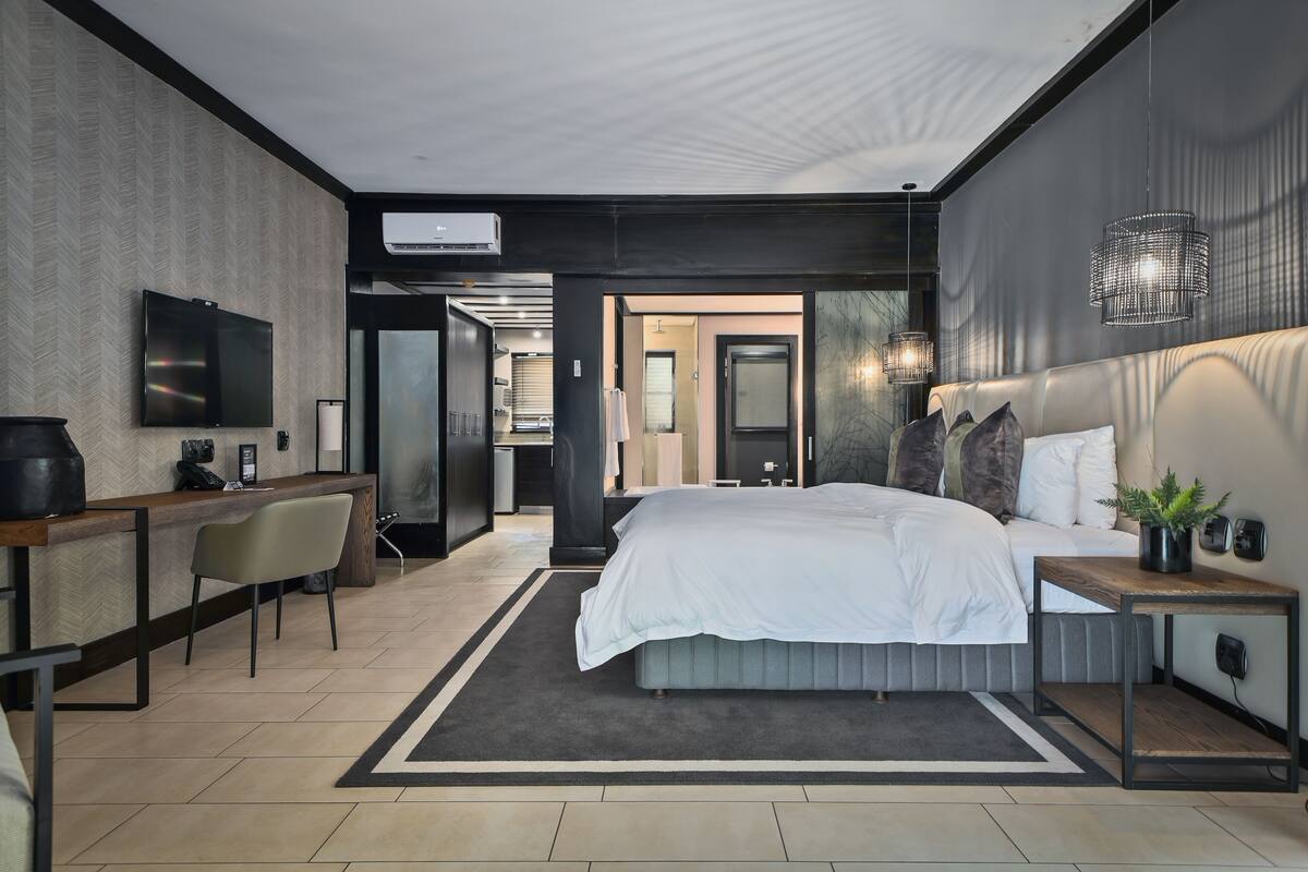 A modern hotel room with a large bed, a desk, a chair, and a TV.