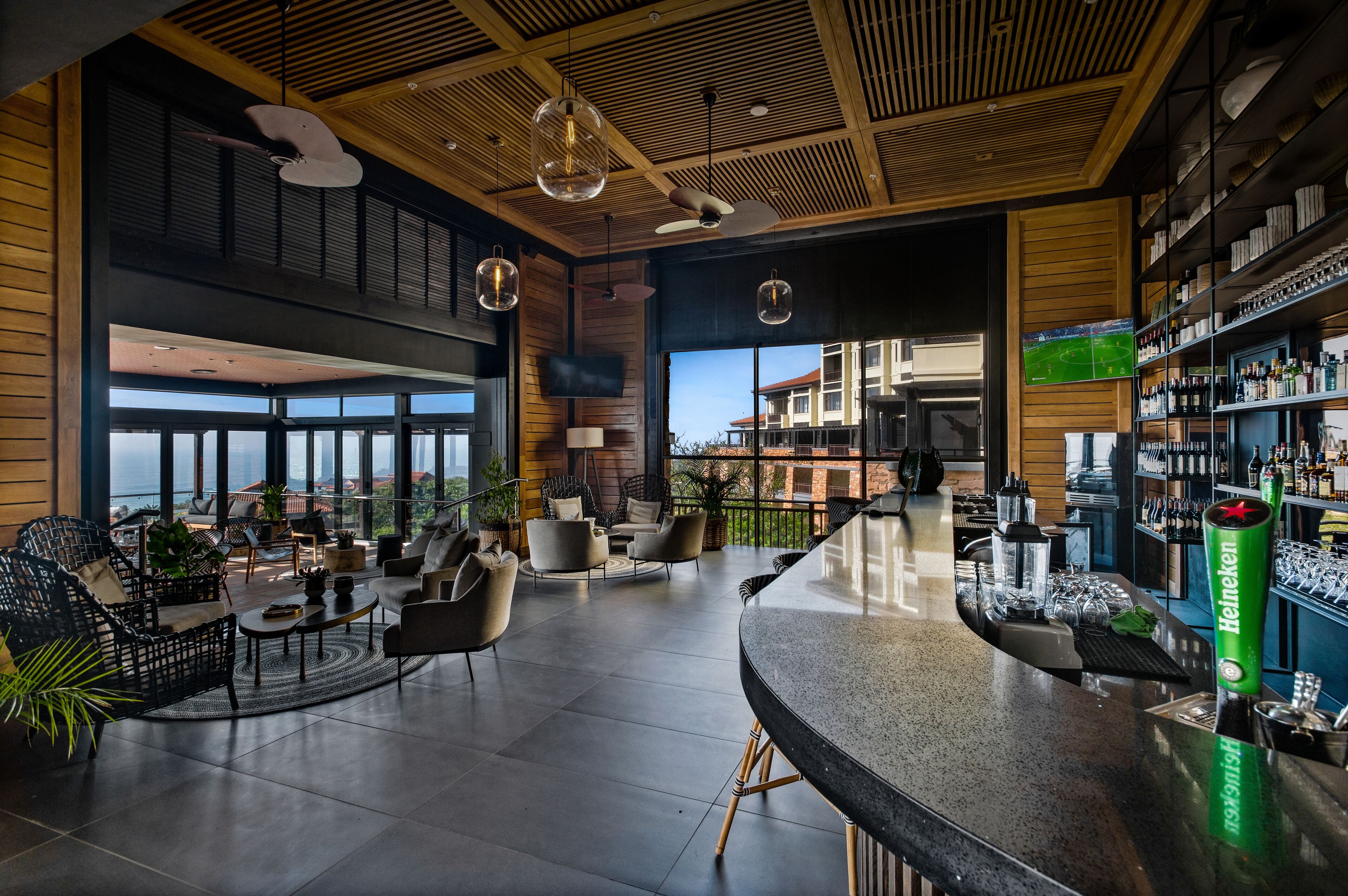Eine moderne Bar mit hoher Decke, Holzvertäfelung und Blick auf die Stadtlandschaft.