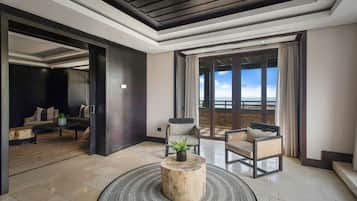 Quarto de hotel moderno com uma varanda grande, área de estar com sofá e cadeiras, e uma mesa redonda de madeira com uma planta.