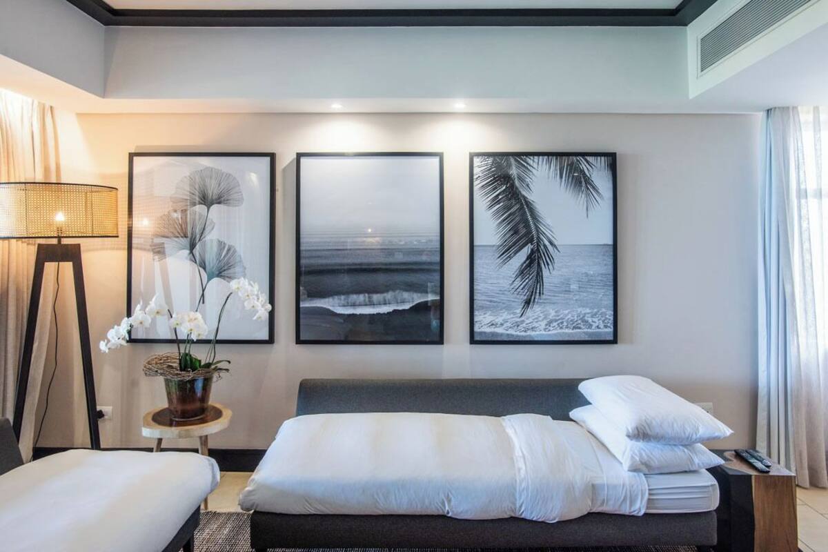 A hotel room with a bed, a side table with a lamp, and three framed pictures on the wall.