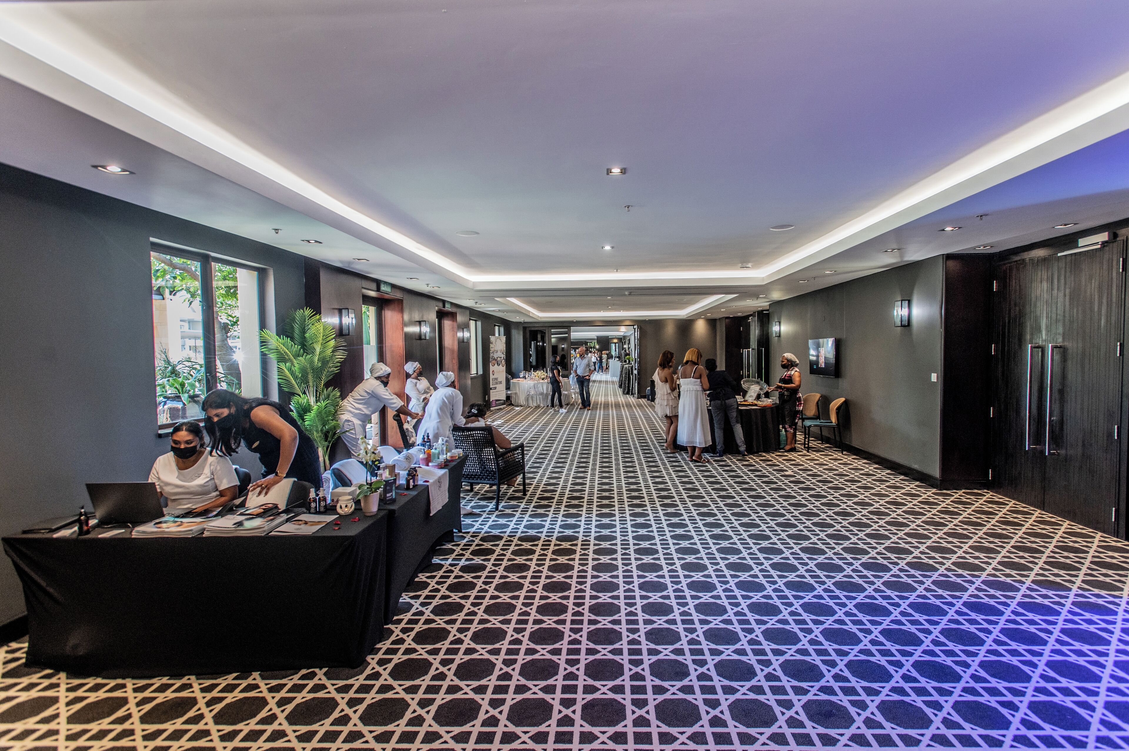 A hotel corridor with a patterned floor, a reception desk, and a TV mounted on the wall.
