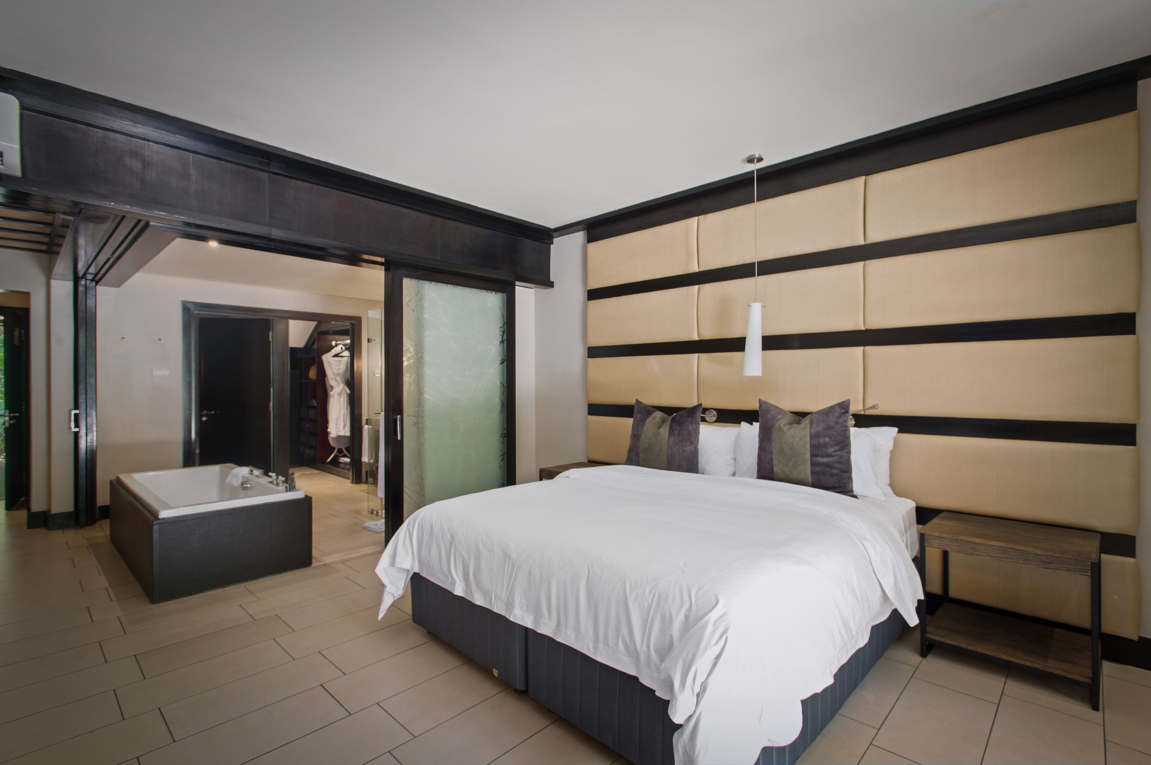 A modern hotel room with a large bed, a separate bathroom with a bathtub, and a walk-in closet.