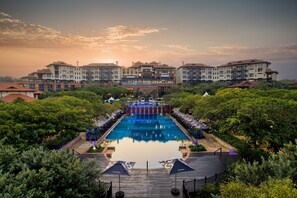 A hotel with a large pool, surrounded by lush greenery and a sunset view. - The Capital Zimbali (Ballito)