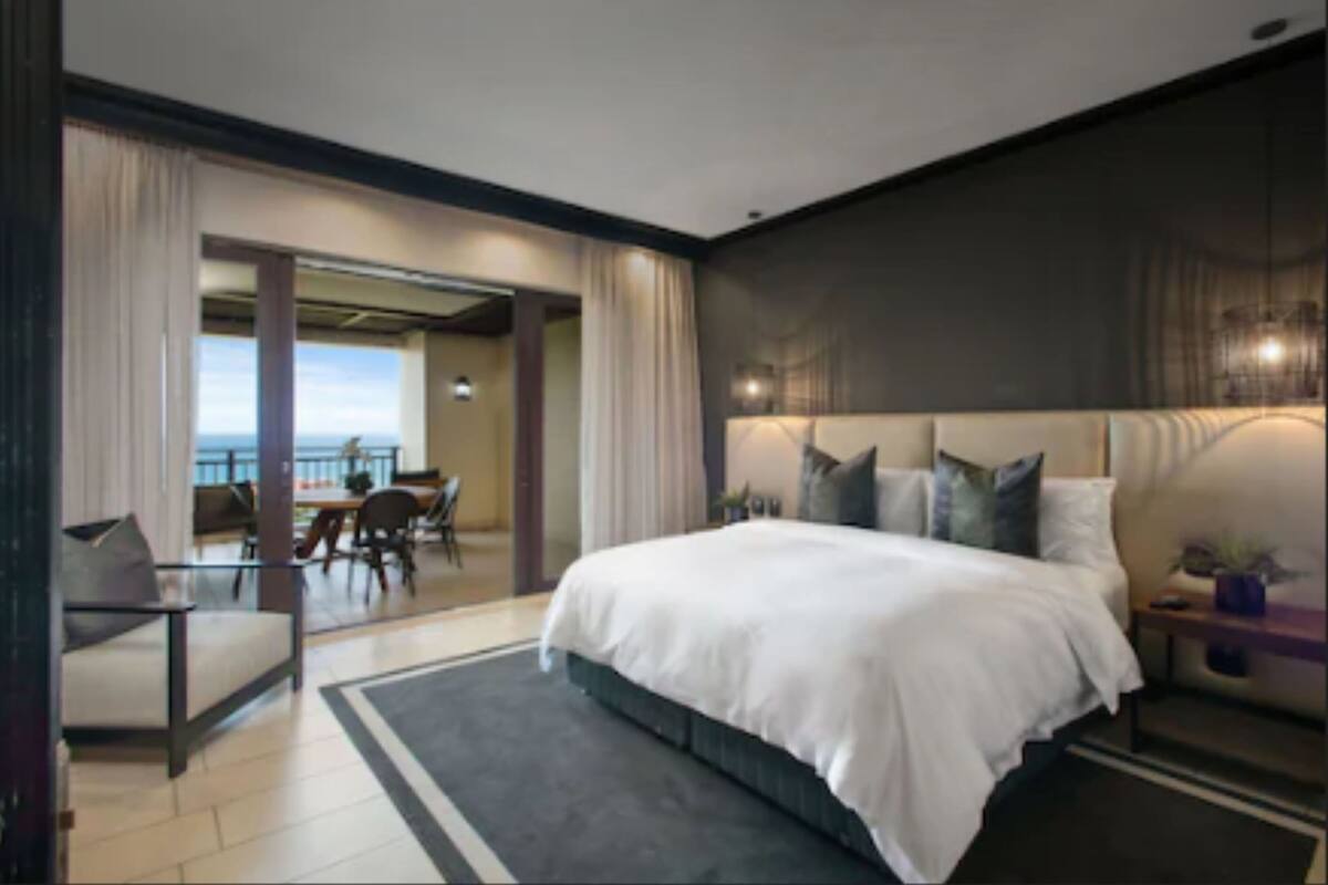 A modern hotel room with a large bed, a seating area with a view, and a balcony.