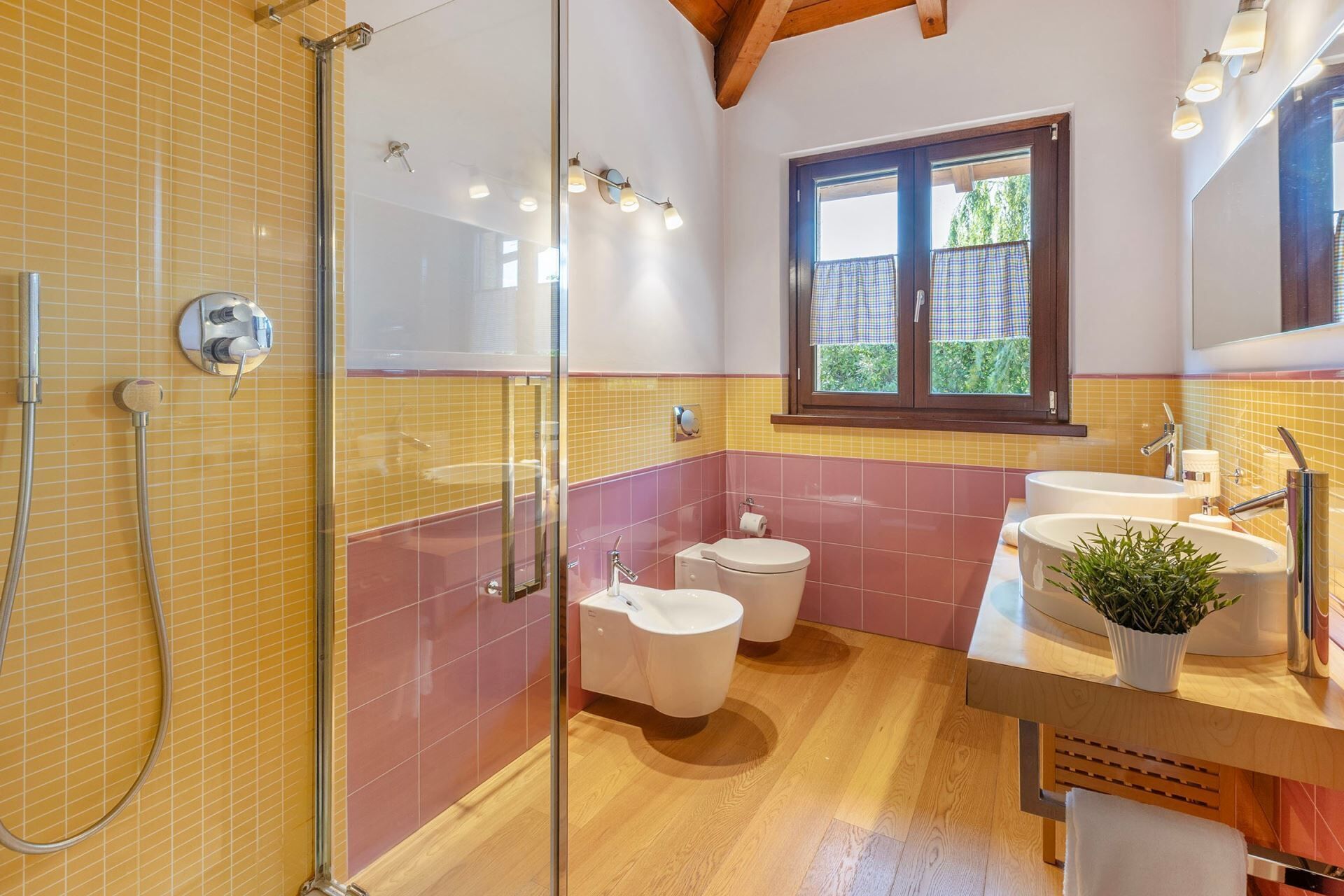 A bathroom with a glass shower enclosure, two toilets, a sink, and a window.